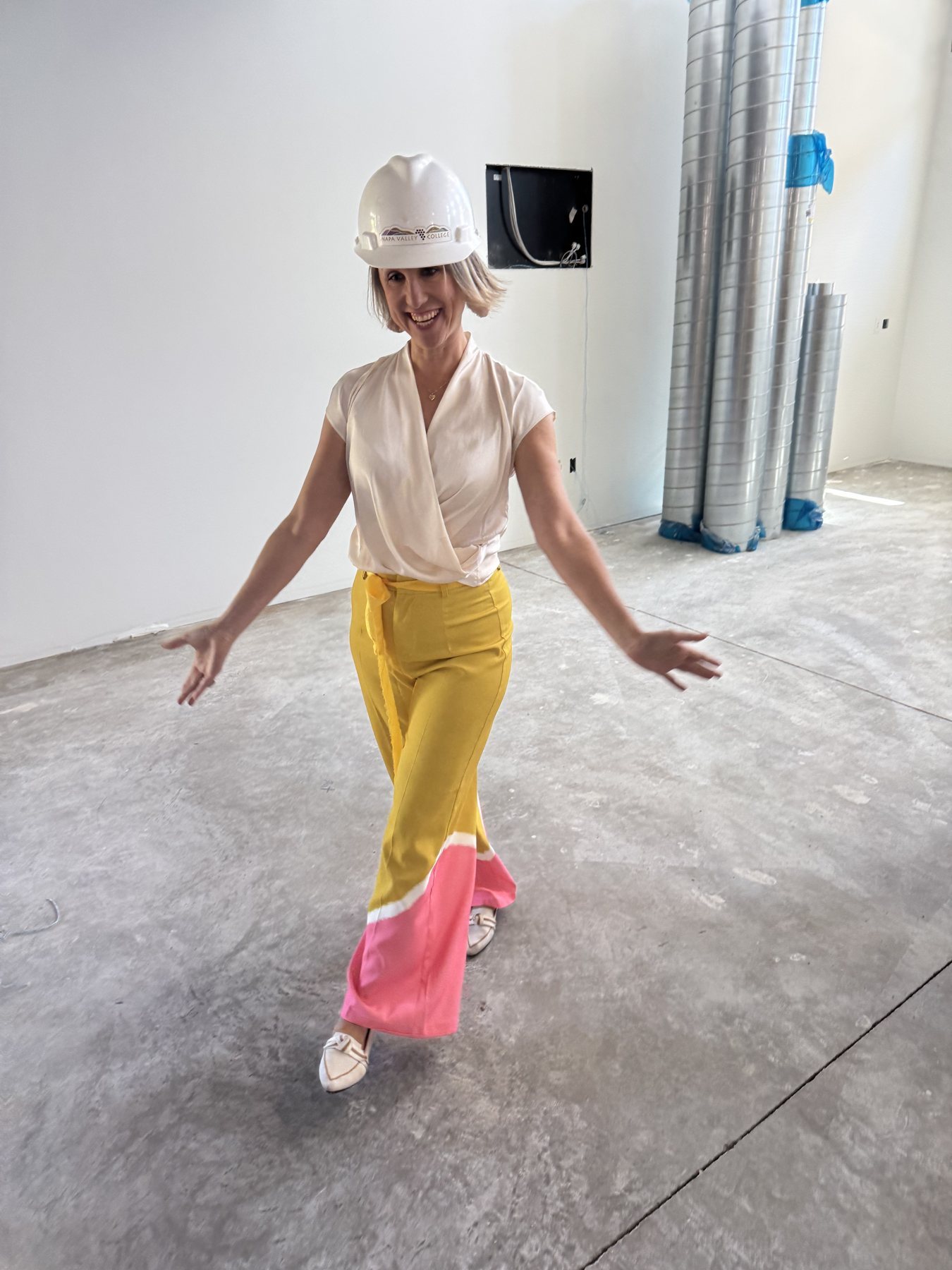 Helene Cornell in a hardhat on a construction site, arms out and smiling